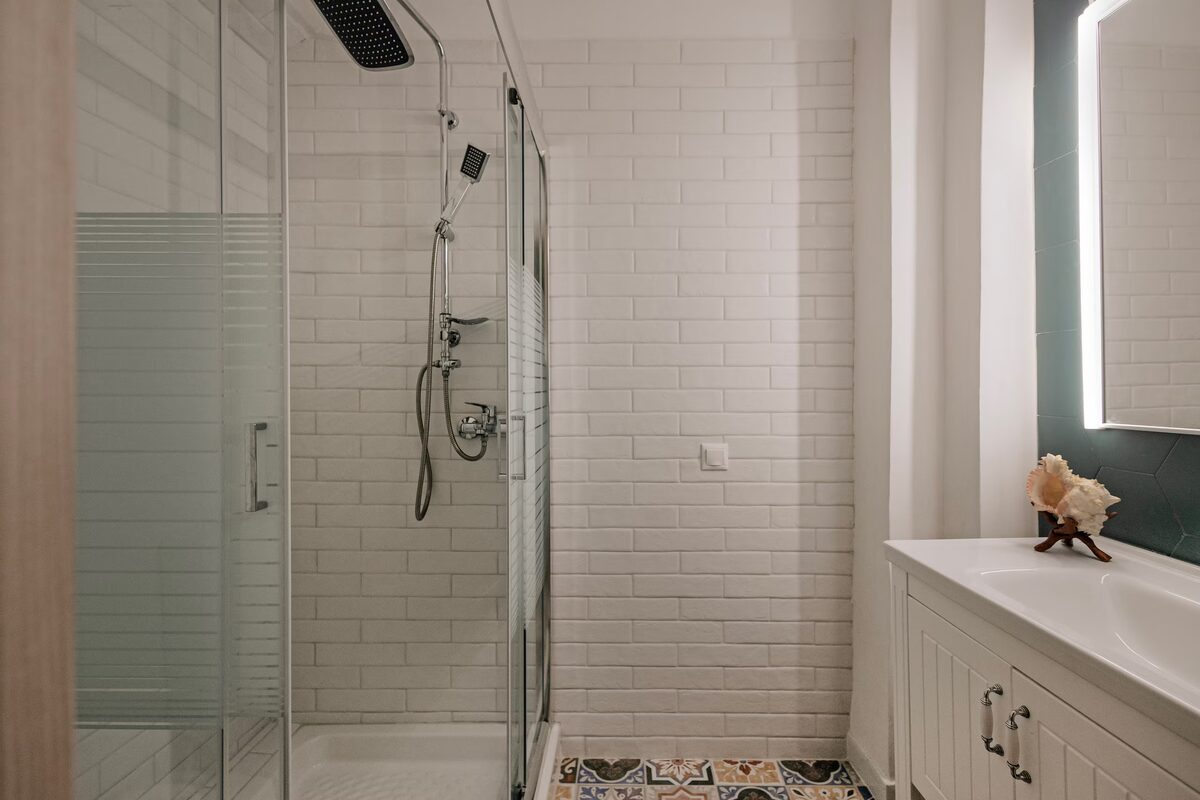 The shower room: a glass walk-in shower, white tiling, patterned floor tiles and a lit mirror.