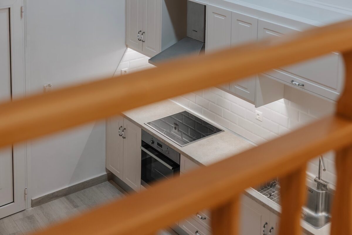 The kitchen along the wall — oven, hob and extractor — seen from the loft through the pine railing.