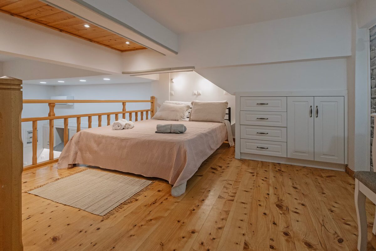The double bed in the wooden loft, tucked under the high ceiling beside the wardrobe.