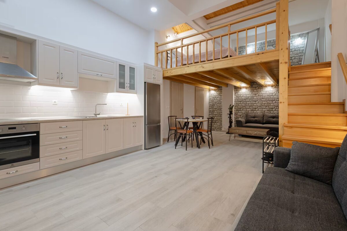The round table and four chairs under the pine beams, with the kitchen running along the wall behind.